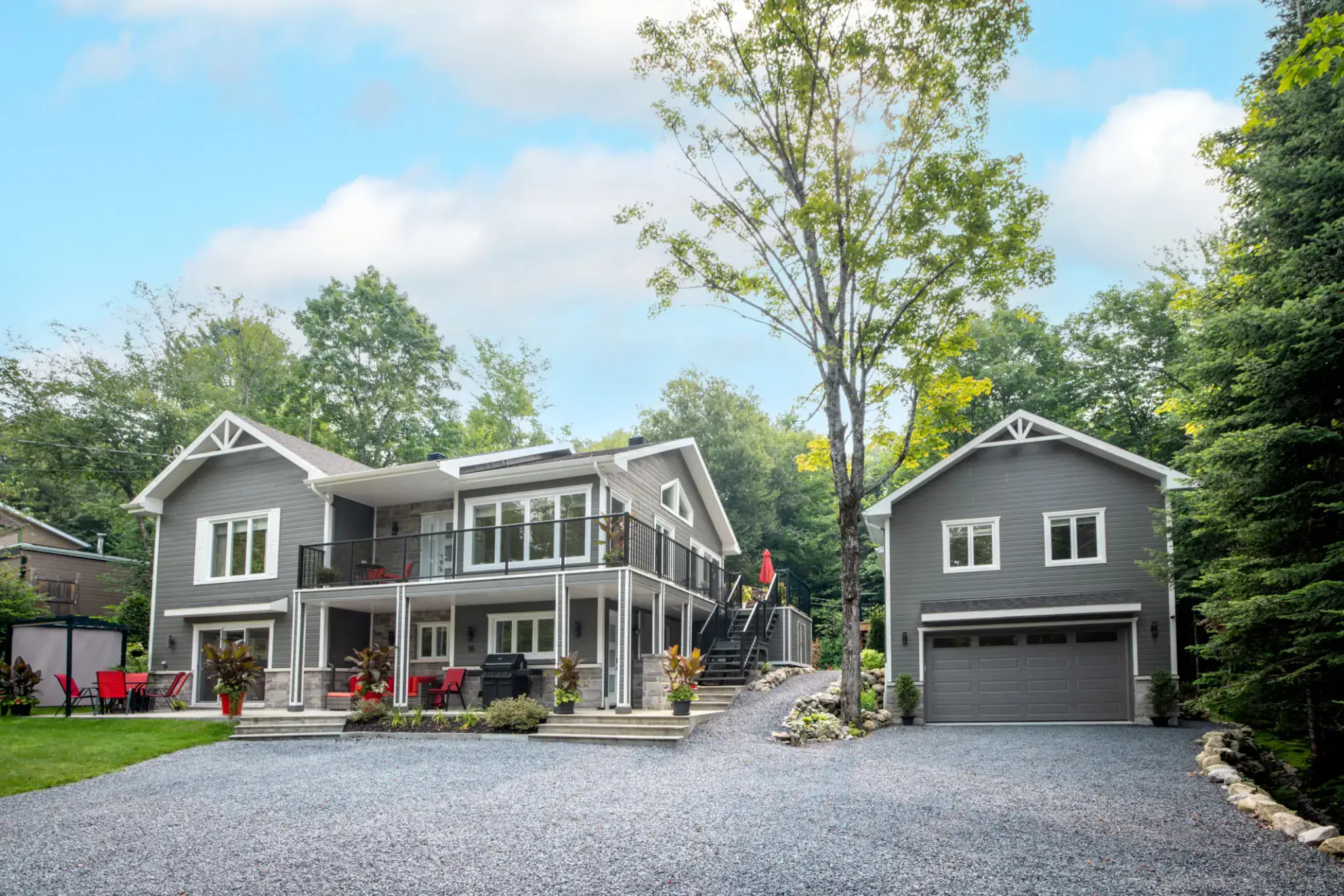 Modern two-story house with gray exterior and detached garage surrounded by greenery.